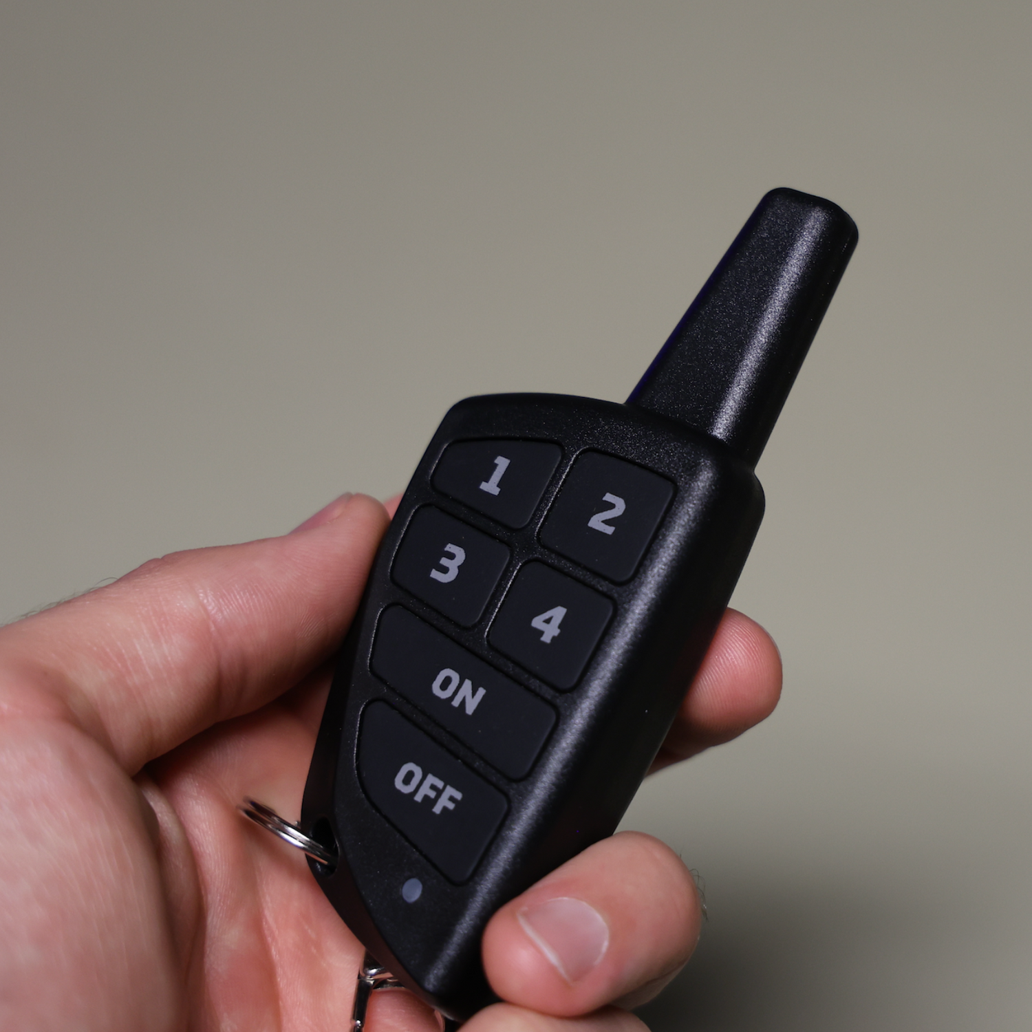 A hand holding a black wireless keyless entry Jahpoo remote fob with a key ring, shown against a plain beige background.